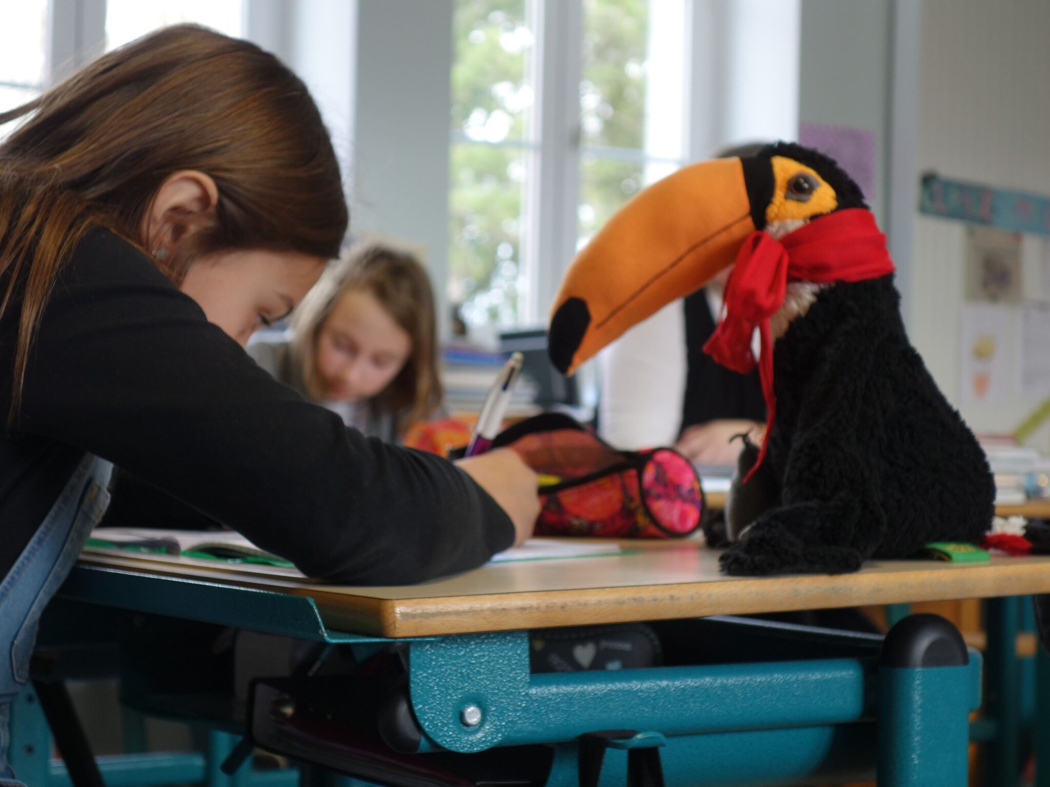 Enfant concentré à son bureau, écrivant dans un cahier aux côtés d’un toucan en peluche 